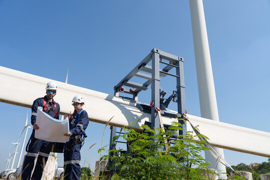 An engineer carefully examines a wind turbine blade at a construction site, placing a large blade on the ground to highlight the renewable energy technology.