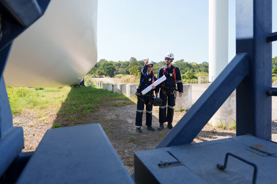 An engineer carefully examines a wind turbine blade at a construction site, placing a large blade on the ground to highlight the renewable energy technology.