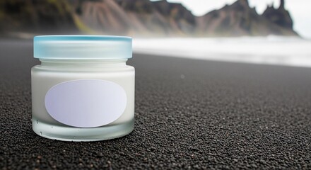 Frosted glass cream jar with a blank white label and blue lid sitting on black volcanic sand at the beach. Arctic spa concept.