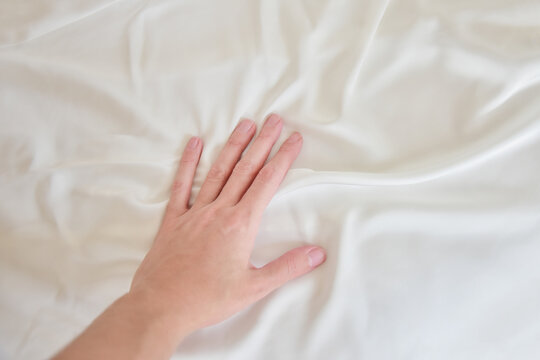 Female hand gently touching white silky sheet