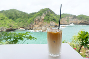 Iced coffee with a view of tropical beach and green hills