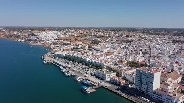Aerial view drone shot of Ayamonte aerial view ayamonte waterfront town midday with calm Guadiana River, whitewashed buildings, marina docks, moored boats, clear blue water, broad promenade,
