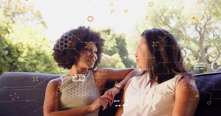 Two women sitting dark couch in garden left woman gesturing starting moving IT overlay showing chat