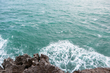 Elevated close-up shot capturing the vibrant turquoise ocean water crashing with great force against dark cliffs. Power, nature's raw energy, and coastal erosion.