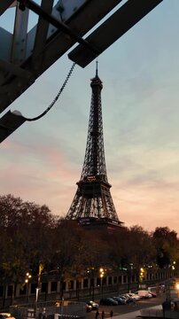 Unique low-angle perspective of the Eiffel Tower at dusk, artfully framed by a stark industrial bridge structure, contrasting iconic beauty with raw urban elements.
