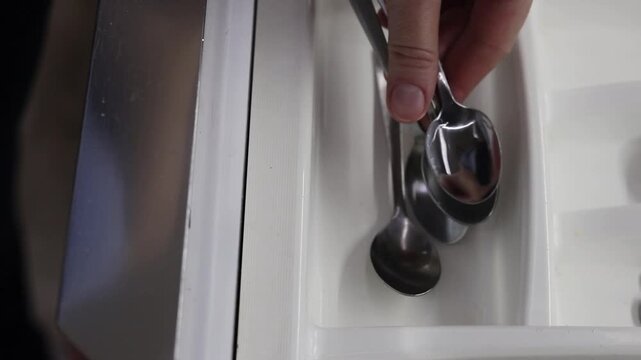 Folding teaspoons into a kitchen cutlery organizer. Clean spoons are folded into a cutlery tray, close-up. Kitchenware
