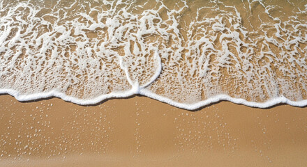 A top-down view of gentle waves lapping on a sandy beach, creating foamy patterns and wet sand textures
