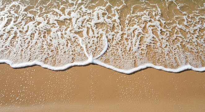 A top-down view of gentle waves lapping on a sandy beach, creating foamy patterns and wet sand textures
