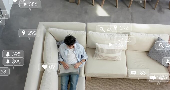 Man sitting on sofa using laptop, posting and receiving social media notifications flooding room