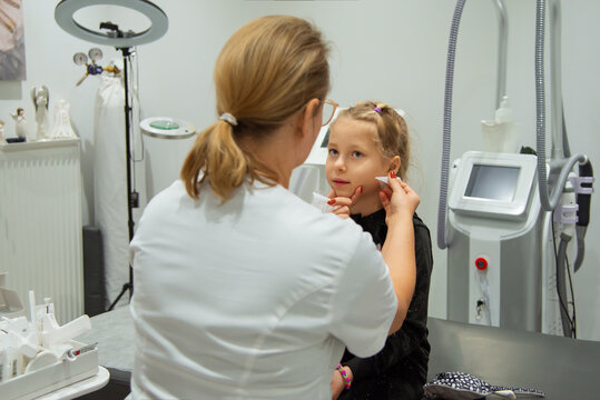 Doctor applying anesthetic to a girl's ear before piercing in a clinic.