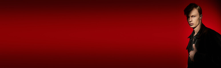 Young man embodies modern masculinity against a striking red backdrop with confidence and allure