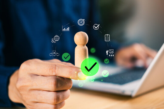 Hand holding wooden figure with digital icons and check marks, symbolizing talent approval, HR evaluation, employee selection, business management - Powered by Adobe