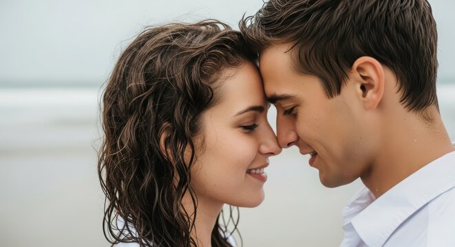 Intimate closeup of a young couple embracing with their foreheads touching, expressing love and connection on a beach