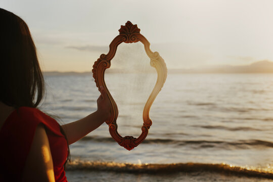 Woman from behind holding a mirror reflecting the sea and waves landscape