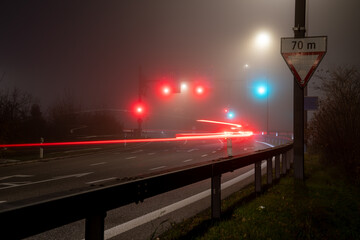Foggy scene with red and green traffic lights at an intersection at night. Red light trails of cars.