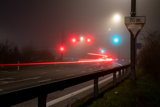 Foggy scene with red and green traffic lights at an intersection at night. Red light trails of cars.