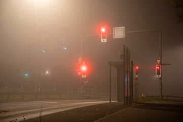 Foggy scene with red and green traffic lights at an intersection and bus stop at night. No cars.