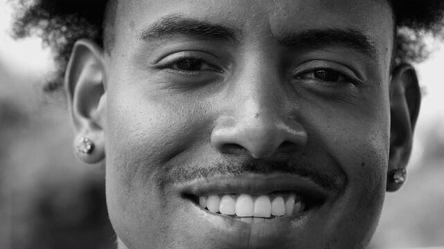 Close-up portrait of young African American man smiling confidently, eyes full of warmth and friendliness, relaxed expression conveying charisma and optimism, in black and white