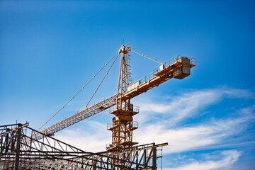tower crane on a construction site, metal framework, against the blue sky with clouds