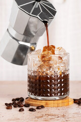Brew coffee pouring into a glass with ice, summer fresh drink iced americano brewed coffee on a beige stone background