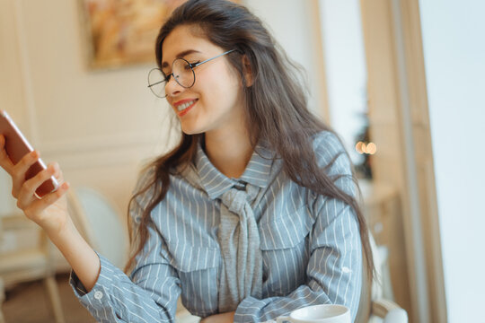 Cafe city lifestyle woman on phone drinking coffee texting text message on smartphone app sitting indoor in trendy urban cafe. Cool young modern mixed race Asian Caucasian female model