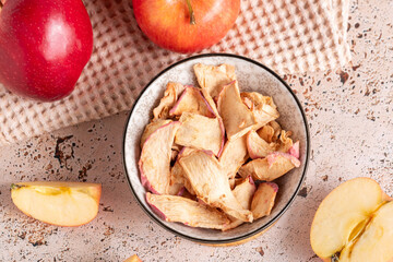 Dried red apple slices in ceramic bowl with fresh apples on a beige napkin on sunny day. Sun-dried natural apple slices on a begie kitchen table background. Healthy snack, top view