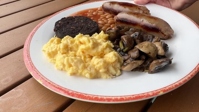 Serving a British Breakfast of Scrambled Eggs, Baked Beans, Blood Pudding and Sausages