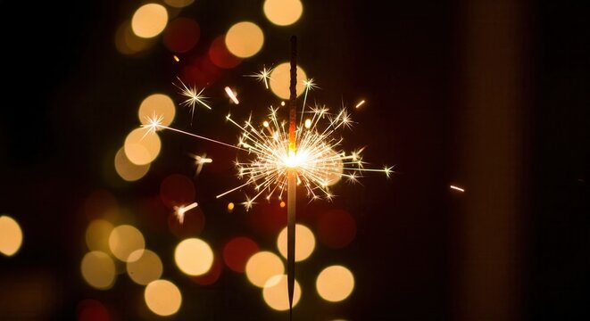 A close-up of a burning sparkler showering sparks. The festive, magical mood is enhanced by warm bokeh lights. Ideal for holidays, celebrations, New Year's Eve, or party themes.