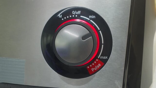 A hand adjusts the illuminated speed dial on the control panel of a food processor to the "max" setting. The modern appliance is used to blend ingredients for cooking or baking.