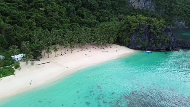 A 4K aerial drone shot descending and moving forward toward Seven Commandos Beach in El Nido, Palawan. The clip captures crystal-clear turquoise water and a tropical shoreline lined with palm trees