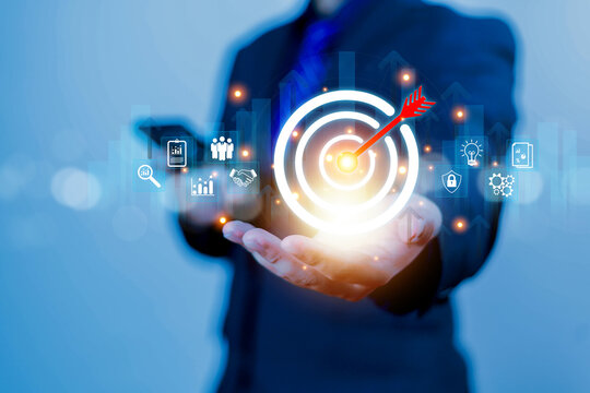 Businessman holding a glowing digital target with an arrow in the center, symbolizing business goals, strategic planning, marketing focus, data analytics, successful achievement in modern technology.