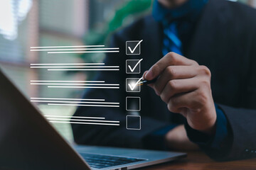 Businessman marking a digital checklist on a laptop, representing task management, project...