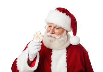 Naklejka premium Santa claus wearing his traditional red suit and hat, holding and looking at a christmas cookie, isolated on transparent background