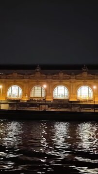 Wide night view of Mus&eacute;e d'Orsay with illuminated facade and glowing clocks.