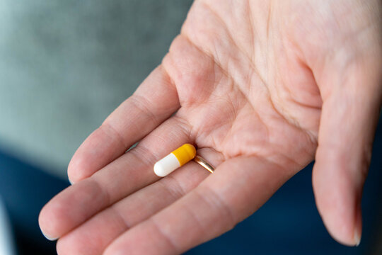 Hand of a person holding a yellow and white capsule pill, showcasing the importance of medication adherence and health management in daily life and wellness routines