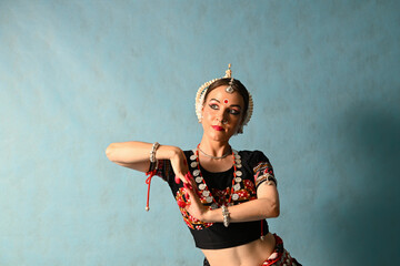 An Indian dancer girl poses in a dance pose in a studio on a blue background