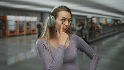 Woman wearing headphones in airport making gesture with finger to indicate she is watching the surroundings, adding a playful element to the busy indoor travel atmosphere.