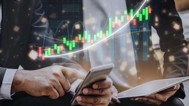 Businessman engaged in financial analysis using smartphone and tablet while stock market graphs display on a digital screen in a modern office atmosphere. Copula