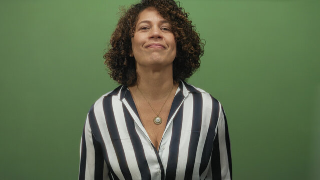 Woman smirking while fingers form l gesture on forehead in green studio wearing striped blouse; playful mockery.