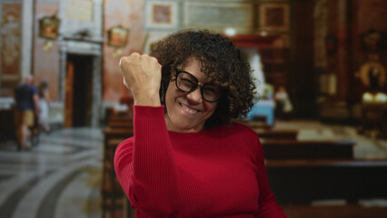 Woman raising fists in a church building interior with wooden pews, altar and ornate wall art;...
