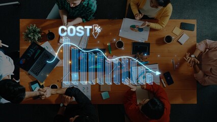 A high-angle view of a business meeting where a team engages in cost analysis, showcasing graphical data visuals and collaborative decision-making around a wooden table. Raster