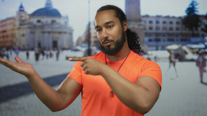 Man wearing orange shirt pointing finger to open palm on street in st peters square building; curiosity guidance.