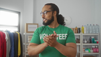 Man in volunteer shirt claps hands in a donations building while smiling and organizing supplies on shelves; community support gratitude.