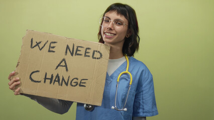 Woman nurse wearing blue scrubs holds cardboard sign reading we need a change in studio; hope...