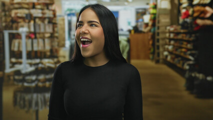 Woman smiling joyfully in a clothing store surrounded by shelves, capturing an indoor shopping experience highlighting fashion and retail with a young latin female in focus.