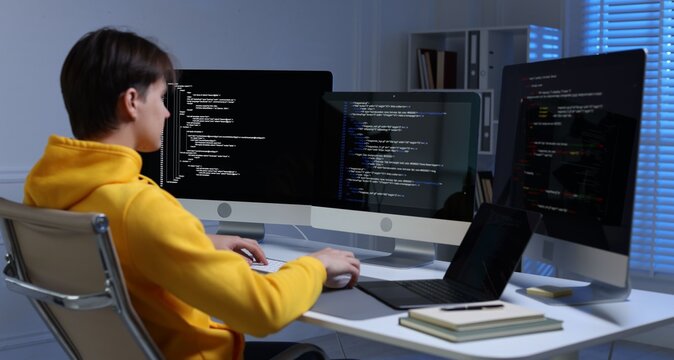 Programmer working on computer with triple monitors and laptop at white table in office