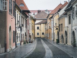 Narrow cobblestone street in Sopron, Hungary, lined with colorful historic buildings, arched doorways, and traditional lanterns on a quiet, overcast day.