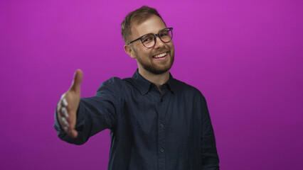Man smiling and extending hand for handshake in studio with vivid purple backdrop wearing glasses; friendly greeting.