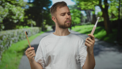Man holding a bamboo toothbrush and an electric toothbrush on a forest path while comparing...