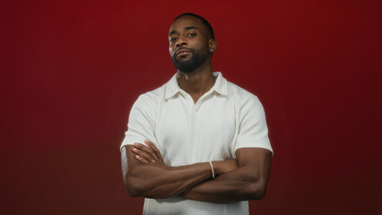 Obraz premium Man with arms crossed showing forearms and bracelet in studio with red backdrop and white polo shirt; calm confidence.
